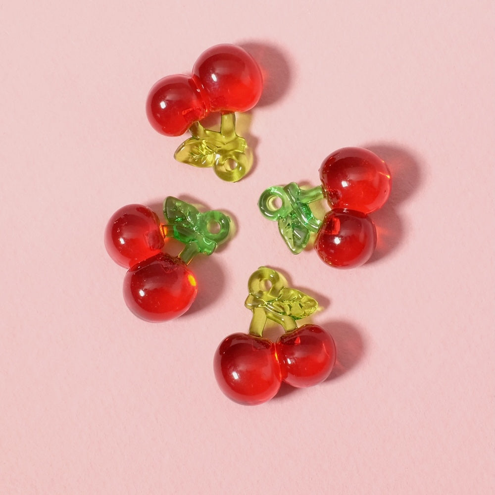 Deux petits pendentifs cerise en acrylique transparent rouge avec des tiges vertes.