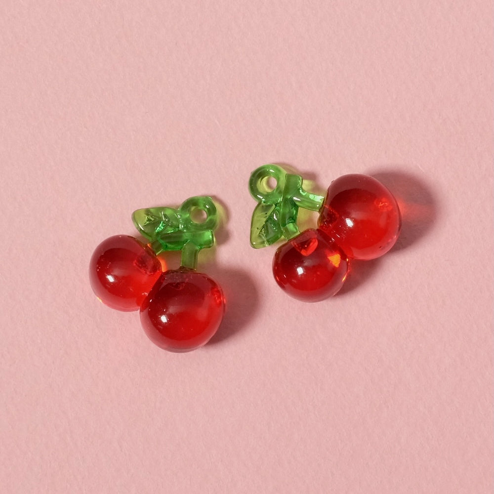 Deux petits pendentifs cerise en acrylique transparent rouge avec des tiges vertes.