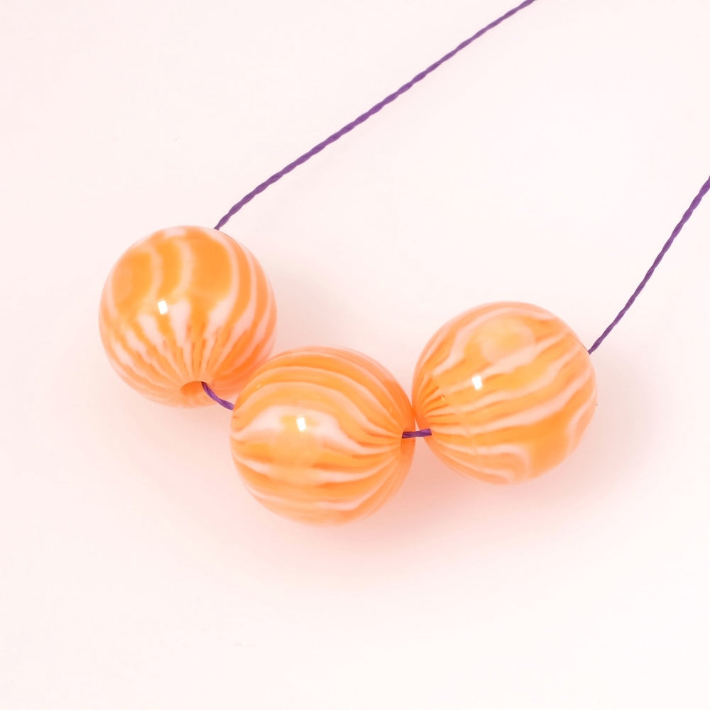 Trois perles rondes en acrylique orange et blanc opaque sur un fil.