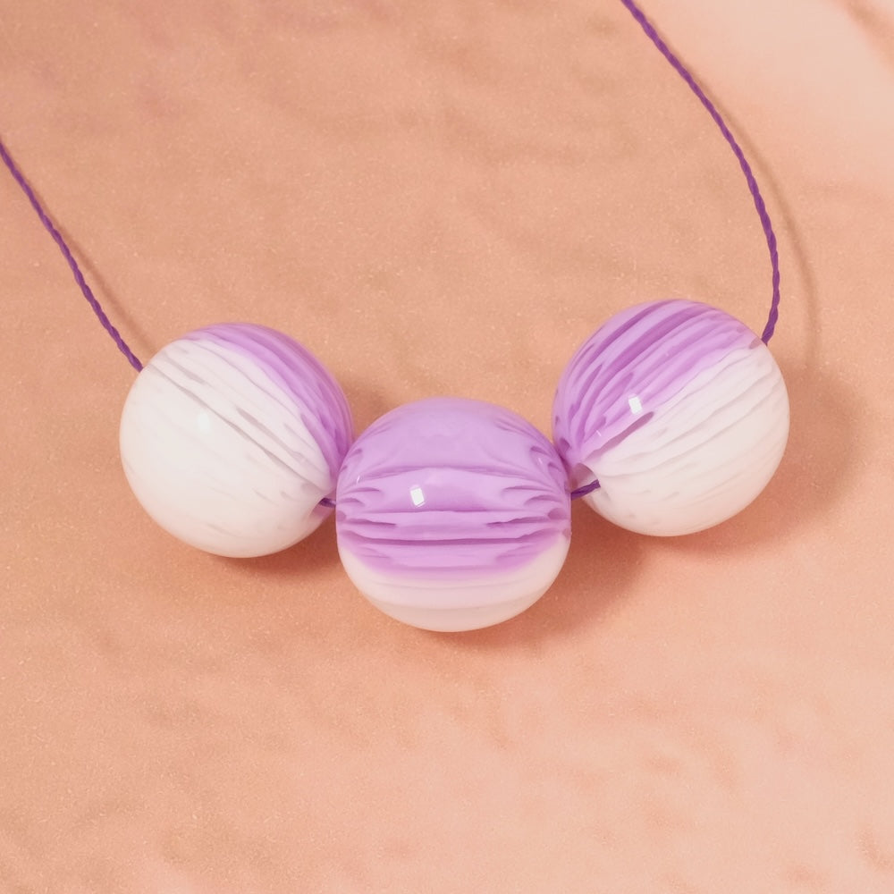 Trois perles rondes en acrylique violet et blanc avec un motif strié.