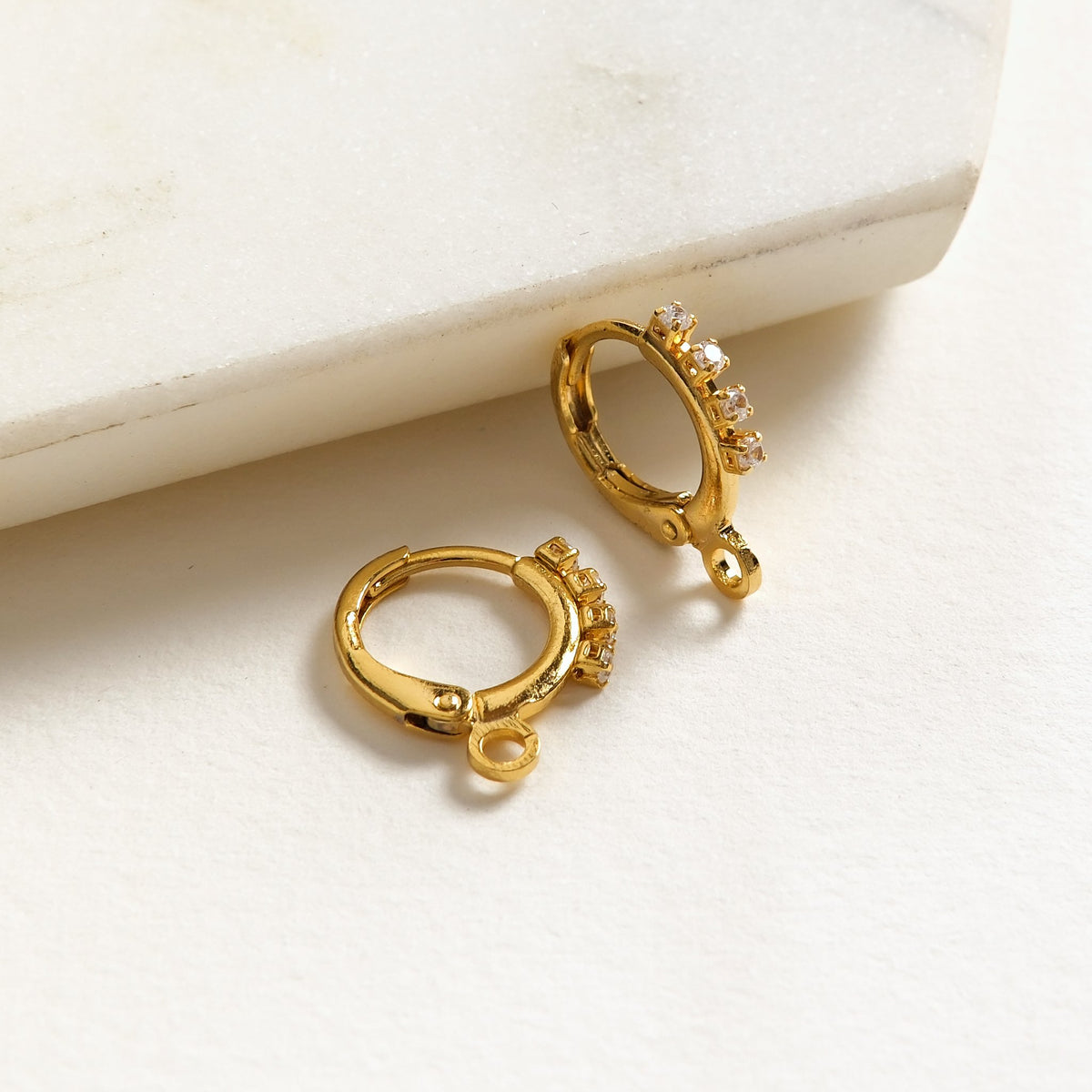 Paire de boucles d'oreilles dormeuses rondes à strass dorées à l'or fin 24K posées sur marbre