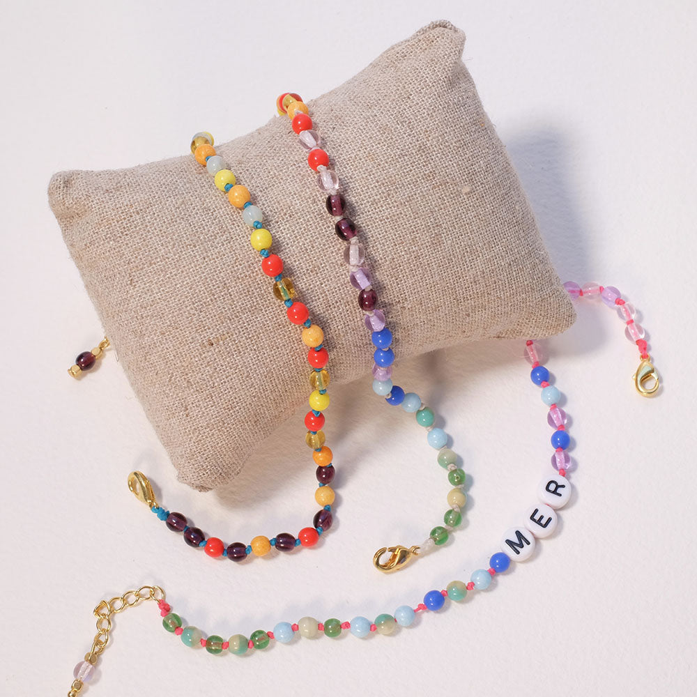 Trois bracelets colorés en perles sont disposés sur un petit coussin beige.