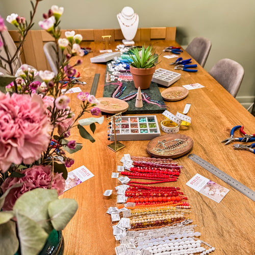 Table de création de bijoux avec perles, outils et fleurs.