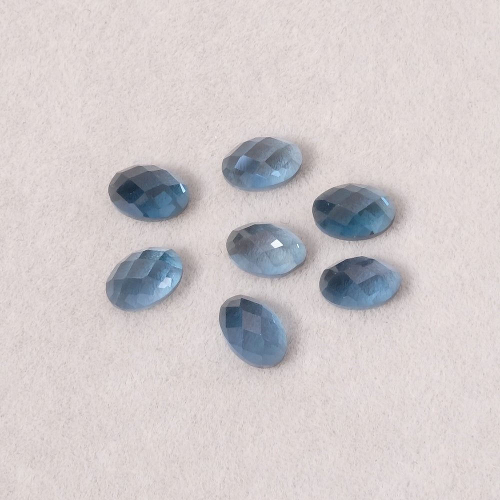 Sept topazes bleues ovales facettées sur fond texturé.