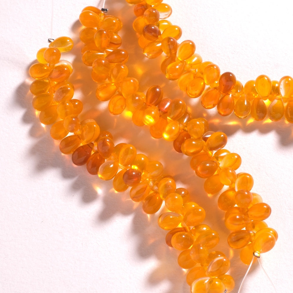 Gouttes de verre orange vif 6 x 9 mm suspendues au fil, formant une frange à contre-jour
