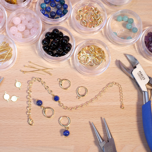 Atelier de création de bijoux avec perles dorées, fermoirs et outils.