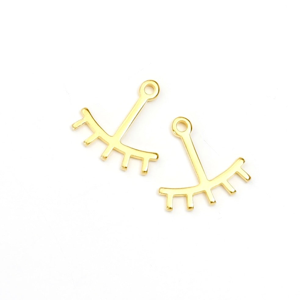 Deux breloques dorées en forme d'œil stylisé avec cils.